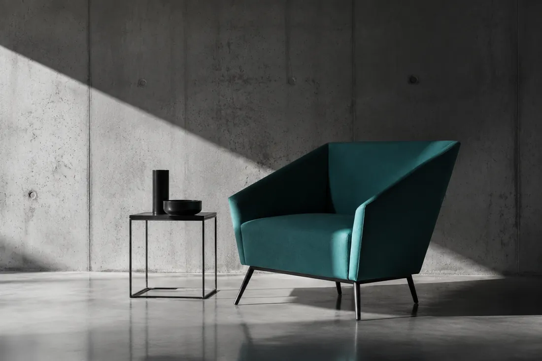 Sillón modular tapizado en verde azulado sobre suelo de cemento pulido